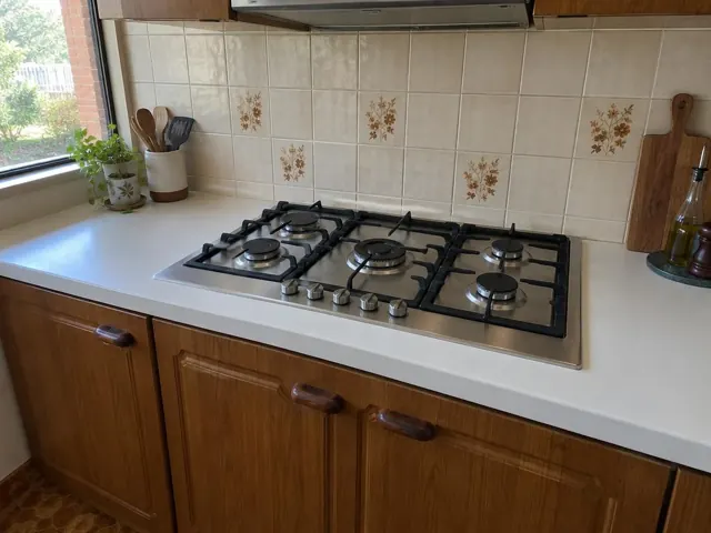 Built-in gas cooktop set into a white kitchen benchtop with tiled splashback and timber cabinets in Woodberry
