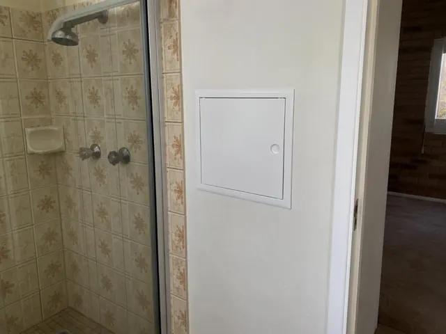 Bathroom shower wall with a small white access panel beside tiled shower in Ashtonfield